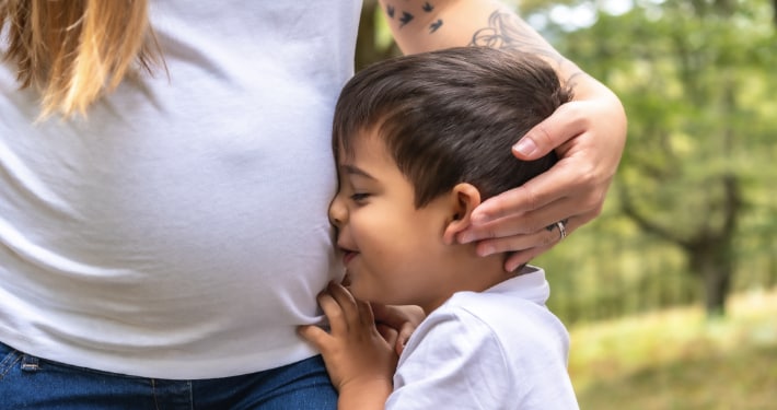 Small boy presses his face against his pregnant mother's side