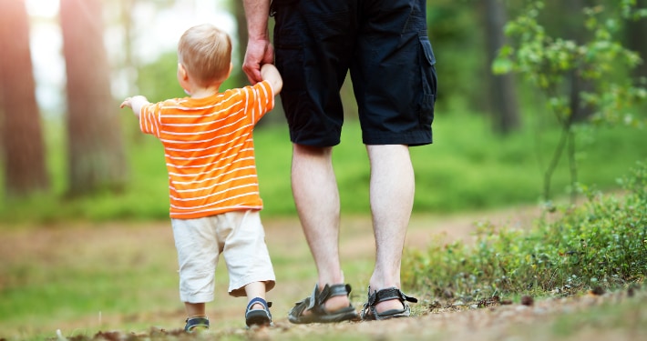 Our Practice A father walks in the woods with his toddler aged son