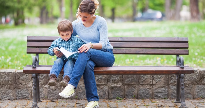 A mother sits on a park bench reading to her son
