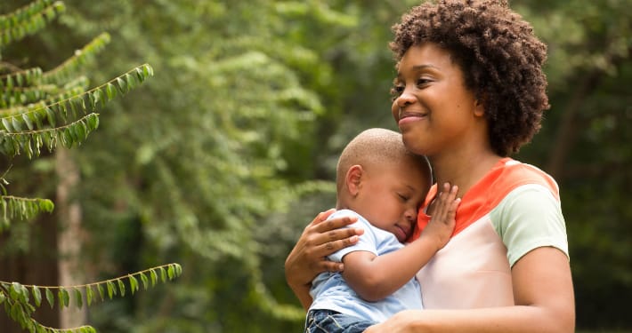 A Black woman holds her infant son to her chest