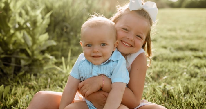 Our Practice A smiling girl hugs her infant brother