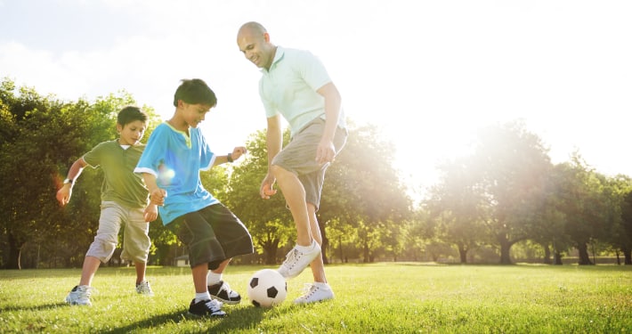 Our Practice A father plays soccer in the park with his sons